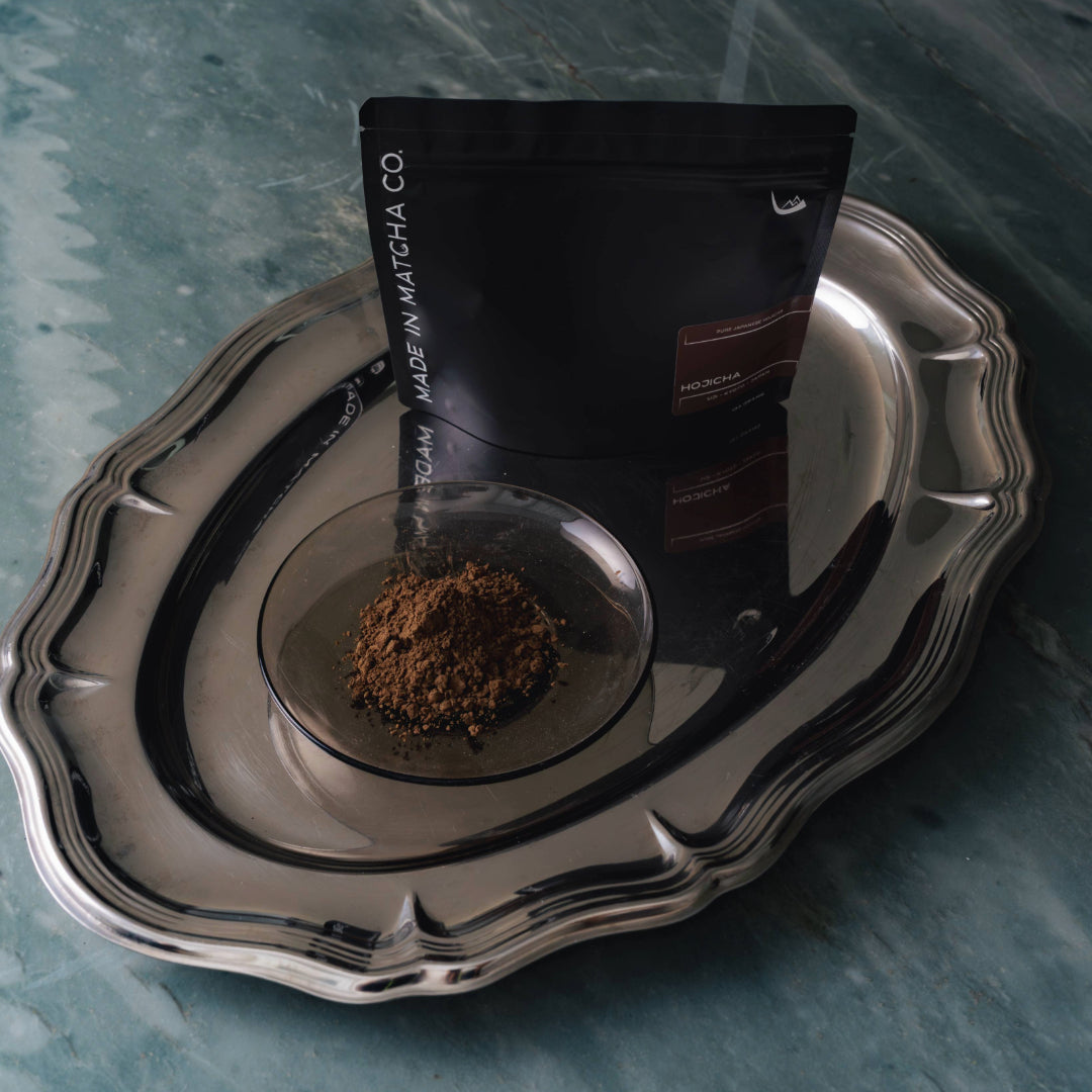 Silver tray with a clear container of ground hojicha powder