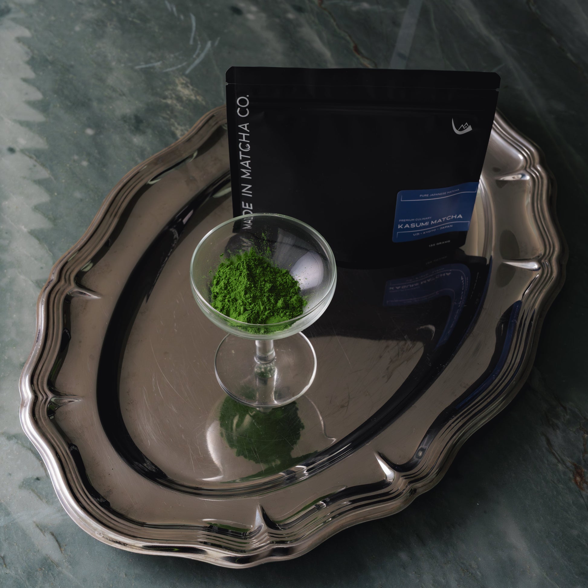 Silver tray with a glass of green matcha and packaging on a marble surface